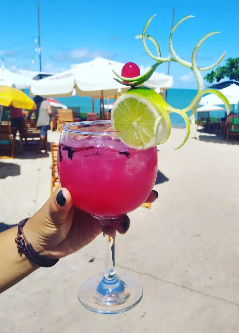 Drink rosa com rodela de limão, com a praia e os guarda-sóis ao fundo